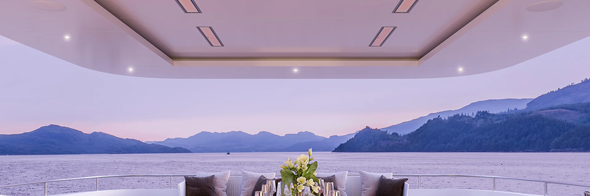 Bromic Platinum Electric Marine heaters recessed in the ceiling of a yacht aft deck at dusk, with forested mountains across the water