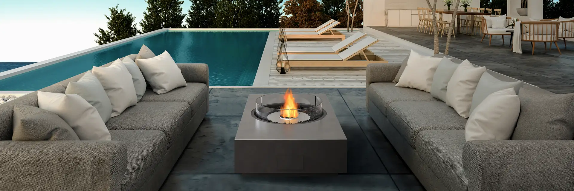 EcoSmart Martini 50 fire table burning between gray sofas on a terrace beside an infinity pool, with pines and the sea beyond
